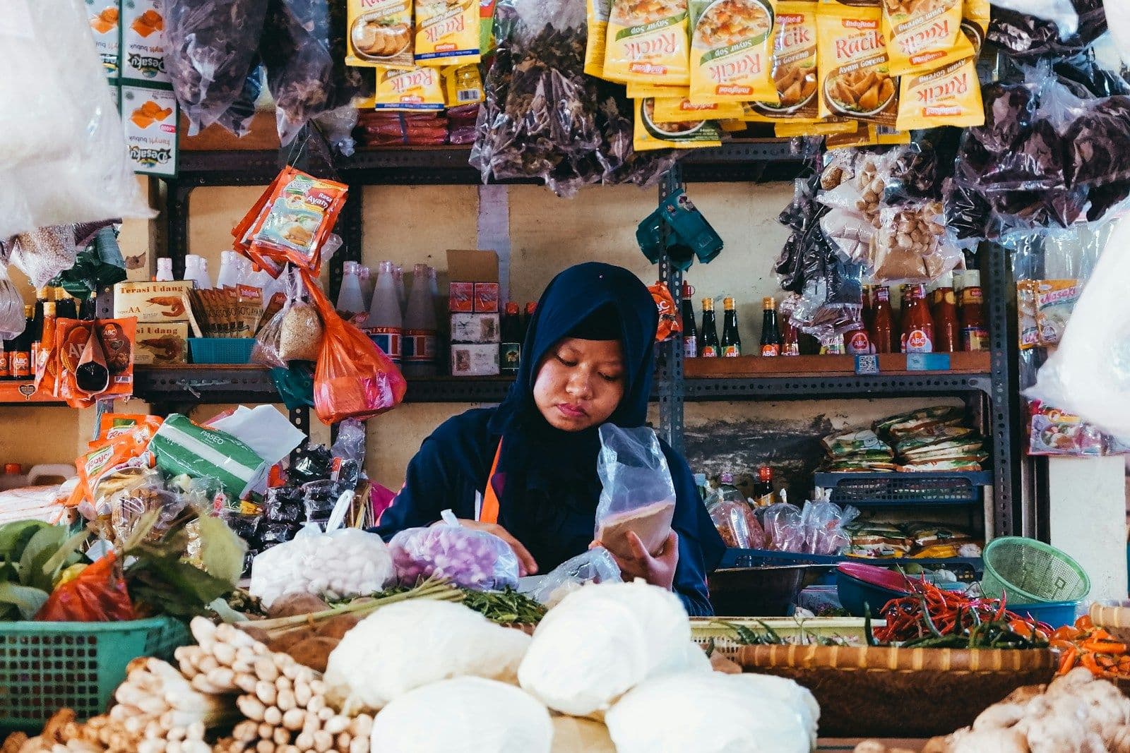 Pemilik toko kelontong berjilbab di antara barang dagangan yang tergantung dan tertata