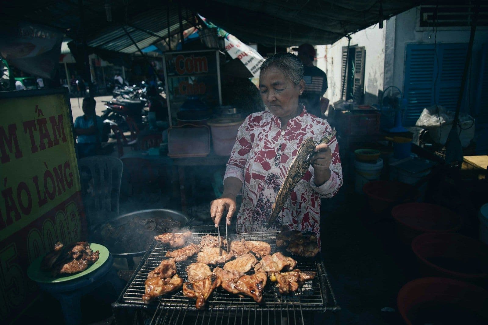 Seorang ibu membakar ayam di atas panggangan di warung makan