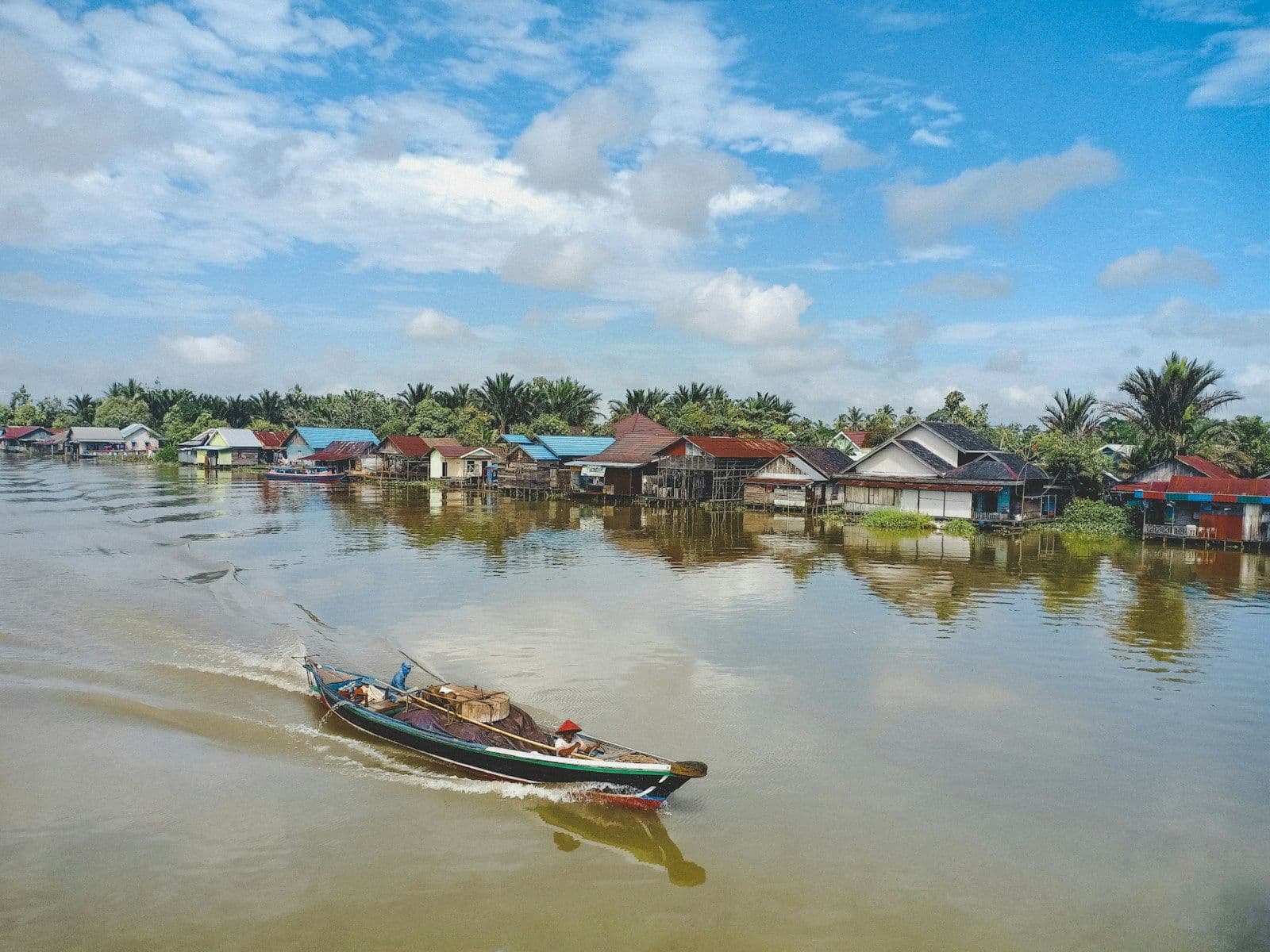Perahu melintas di depan rumah-rumah panggung di tepi sungai Kalimantan